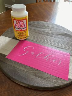 a wooden table topped with a pink sign and bottle of glue sitting on top of it