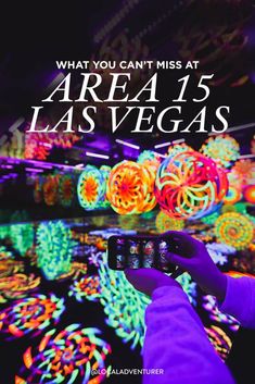 someone taking a photo with their cell phone in front of colorful lights and text that reads, what you can't miss at area 15 las vegas