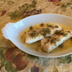 two pieces of fish are in a yellow sauce on a floral tablecloth covered table cloth