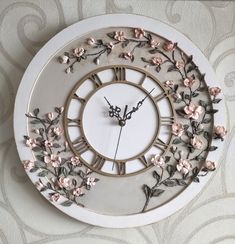 a white clock with pink flowers and leaves on the face is hanging on a wall