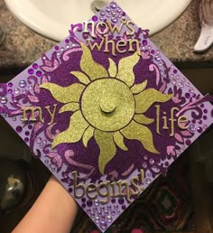 a purple and gold graduation cap with the words now is when my life begins