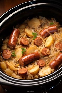 a crock pot filled with sausage, potatoes and sauerkraut on top of a wooden table