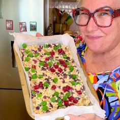 a woman in glasses holding up a large cookie sheet filled with fruit and cereals