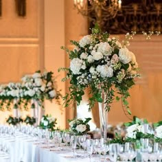 there is a table set up with white flowers and greenery in tall vases