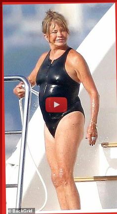 a woman in a black swimsuit standing on a boat with her hand on the railing