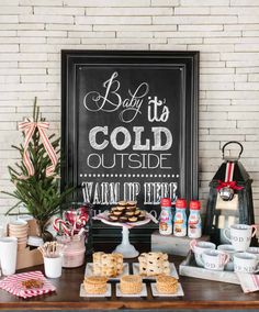 a table topped with cookies and desserts next to a chalkboard that says baby it's cold outside