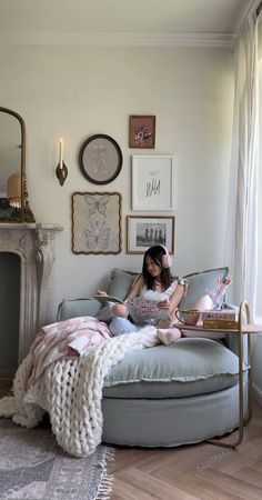 a woman sitting on top of a blue couch in front of a fire place next to a window