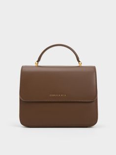 For a simple yet elegant carrier, look no further than this front flap bag. The luxurious dark brown finish lends an air of sophistication to the minimal exterior, creating a polished silhouette that is tastefully adorned with gold-toned hardware. As a subtle detail, the CHARLES & KEITH logo is etched on the front flap. Equipped with a sturdy top handle and detachable shoulder strap, let this bag elevate your outfits no matter how you carry it. Rectangular Flap Bag With Adjustable Handle For Daily Use, Classic Rectangular Flap Bag With Adjustable Handle, Everyday Rectangular Flap Bag With Adjustable Handle, Classic Everyday Box Bag With Adjustable Handle, Modern Rectangular Flap Bag With Adjustable Handle, Elegant Brown Flap Bag With Adjustable Handle, Adjustable Handle Shoulder Bag, Brown Rectangular Flap Bag With Adjustable Handle, Daily Use Flap Bag With Top Carry Handle