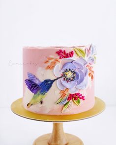 a pink cake decorated with flowers and a hummingbird on top is sitting on a wooden stand