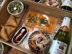 a box filled with food and drinks on top of a wooden table next to bottles of wine