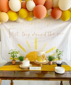 a table topped with cake and balloons next to a white sign that says first trip around the sun