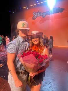 a man and woman standing next to each other with flowers in front of a stage