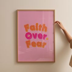 a woman standing next to a pink poster with the words faith over fear written on it