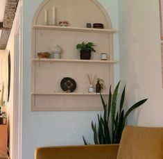 a living room filled with furniture and plants on top of shelves above a doorway leading to a hallway