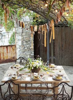 an outdoor dining table set for four under a tree with lights strung from the branches