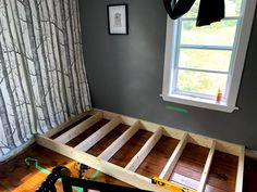 a bed frame being built in a room with wood flooring and curtains on the window sill