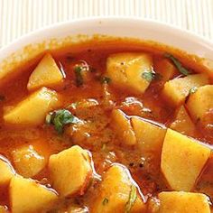 a white bowl filled with stew and potatoes on top of a striped table cloth next to a wooden spoon