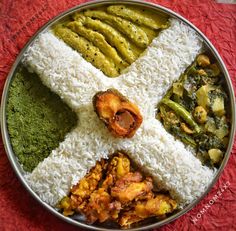 a metal plate topped with rice and different types of food on top of a red table cloth