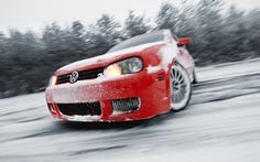 a red car driving down a snow covered road with trees in the backgroud