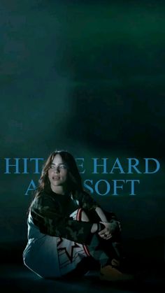 a woman sitting on the ground in front of a sign that says hither hard as soft