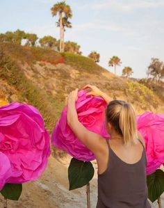 a woman is holding large pink flowers on the beach