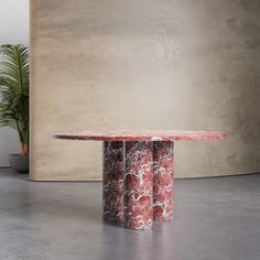 a round table with two red marble pillars in front of a beige wall and potted plant