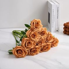 a bouquet of orange roses sitting on top of a white table next to a book