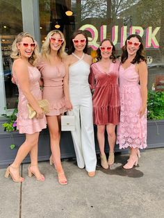 four women in dresses and sunglasses posing for a photo outside of a store front with their arms around each other