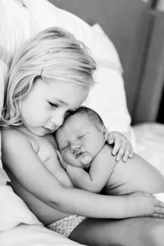 a woman holding a baby in her arms while laying on top of a bed with white sheets