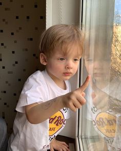 a little boy pointing at the window with his thumb on it's glass door