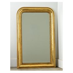 a gold framed mirror sitting on top of a wooden floor next to a white wall