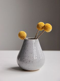 three yellow flowers in a gray vase on a white countertop with grey walls behind it