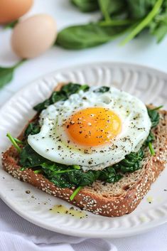 a white plate topped with an egg and spinach sandwich