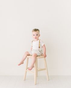 a little boy sitting on top of a wooden chair in front of a white wall