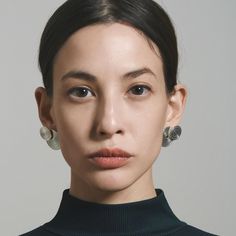 a woman with earrings on her head looking at the camera while wearing a turtle neck sweater