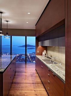 an empty kitchen with wooden cabinets and marble counter tops, overlooking the city lights at night