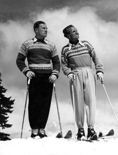 two men standing next to each other on top of a snow covered slope wearing skis