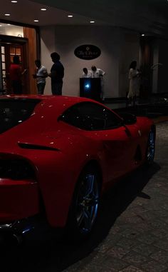 a red sports car parked in front of a building with people standing around it at night