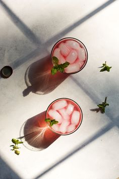 two glasses filled with ice and mint on top of a white table next to each other