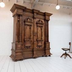 an old wooden armoire sitting on top of a white floor next to a chair