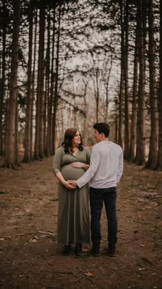 a pregnant couple standing next to each other in the woods