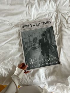 a person holding up a magazine on top of a bed with white sheets and pillows