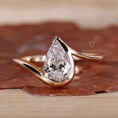 a pear shaped diamond ring sitting on top of a brown leaf covered ground with leaves around it