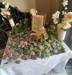 a table topped with rocks and flowers on top of a white cloth covered tablecloth