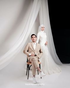 a man and woman sitting on chairs in front of a white curtain, posing for the camera