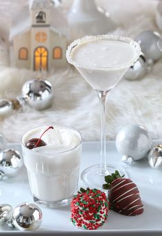 two glasses filled with white wine and strawberries on a tray next to silver ornaments