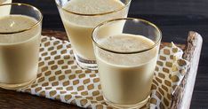 three glasses filled with liquid sitting on top of a wooden tray