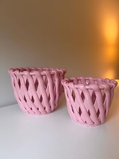 two pink vases sitting next to each other on a white counter top with a light in the background