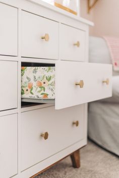 a white dresser with drawers and flowers on the drawer pulls in front of a bed