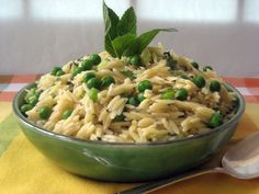 a bowl filled with pasta and peas on top of a yellow table cloth next to a spoon